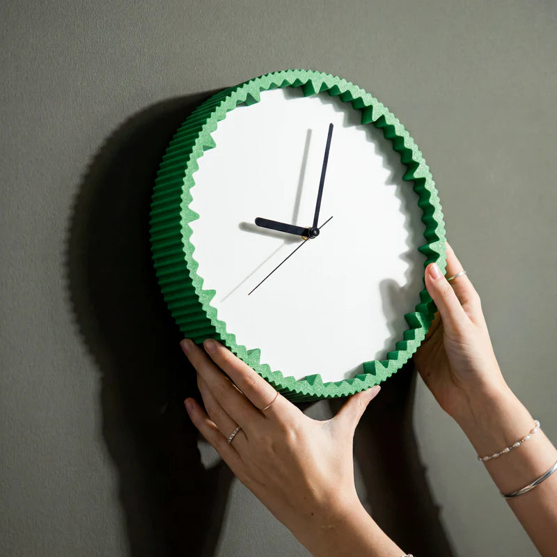 Moderne Wanduhr ZWÖLF in Grün mit Zackenring wird an eine graue Wand gehängt