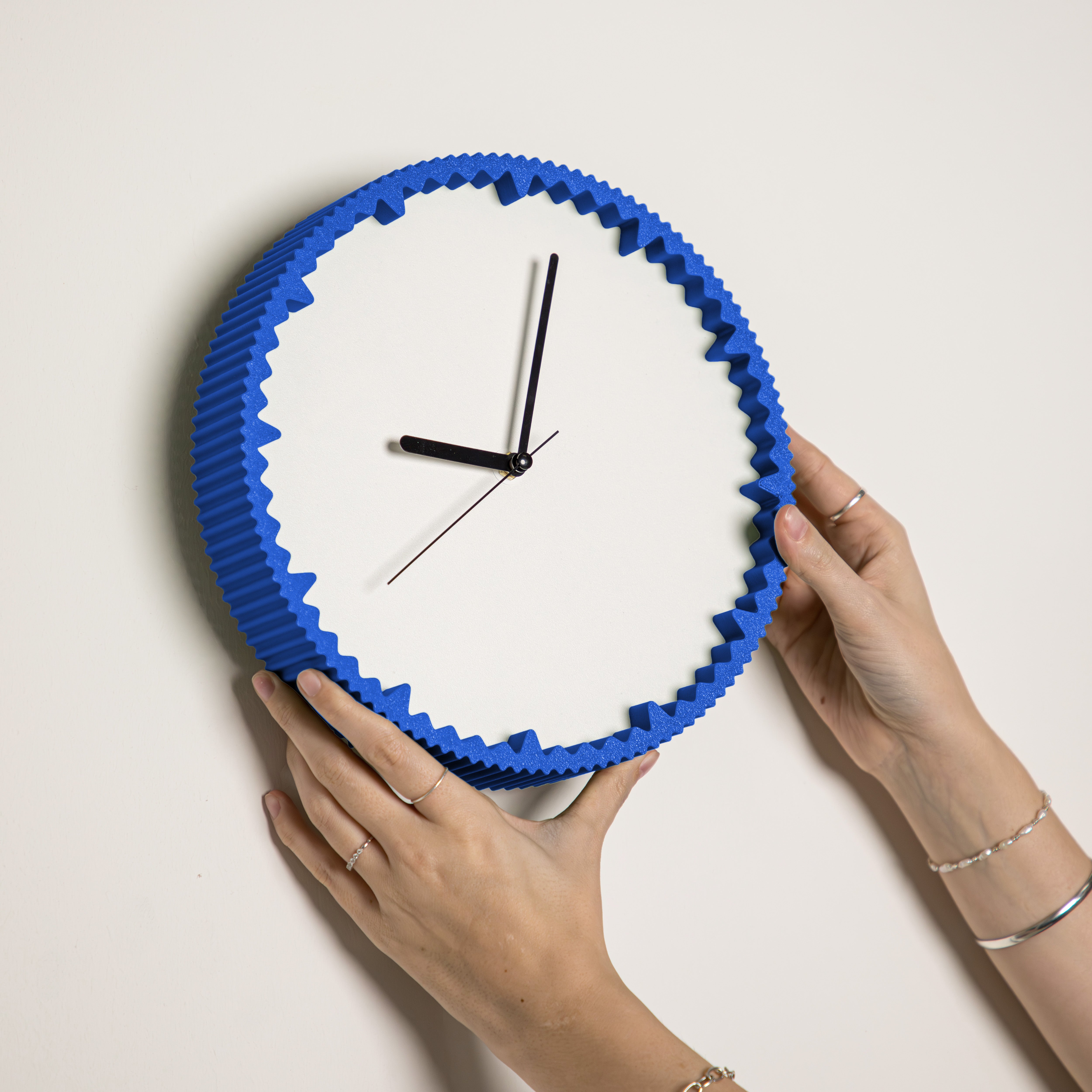 Hände hängen moderne blaue Wanduhr mit gezacktem Rand aus dem 3D Druck an die Wand #farbe_blau