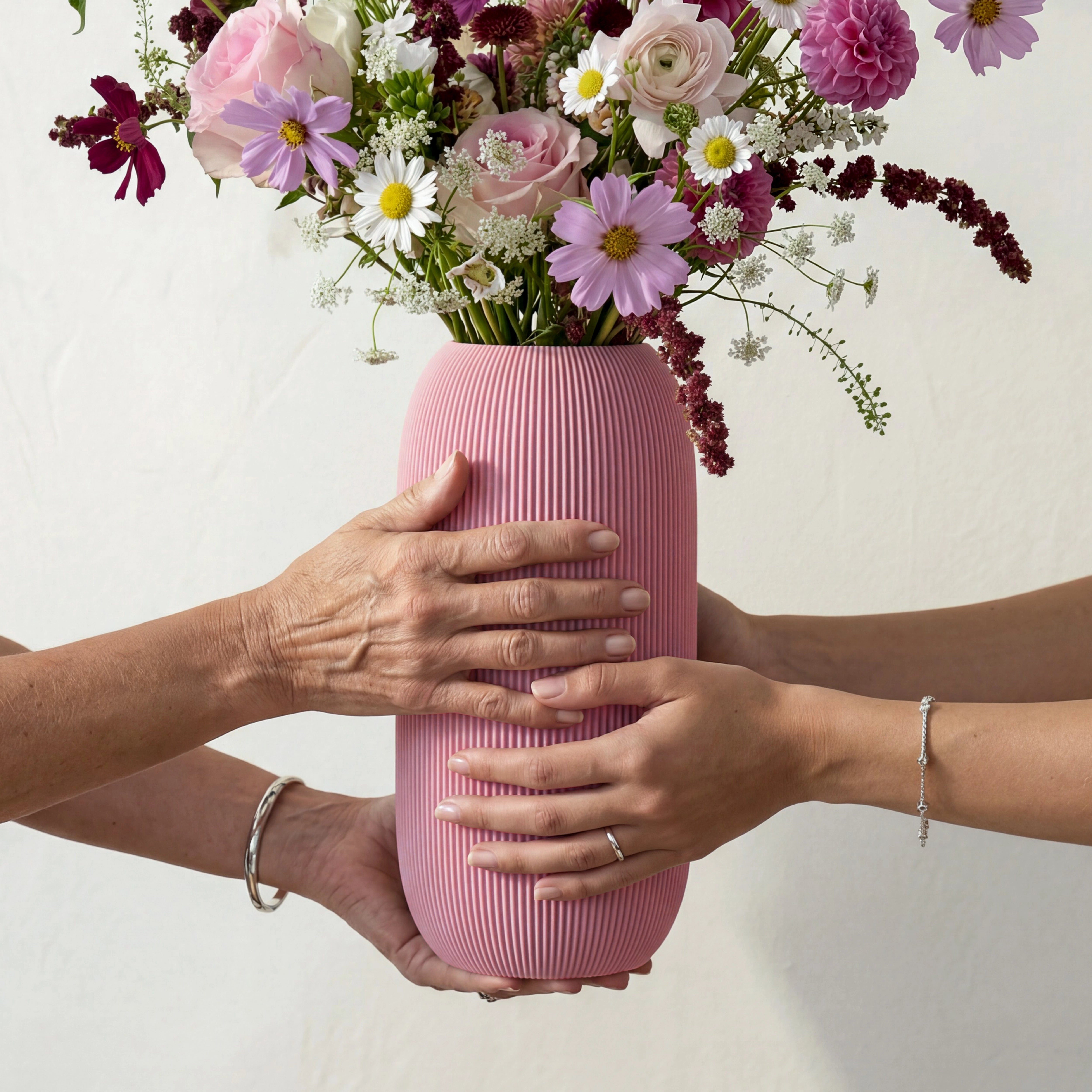 Hände von Mutter und Tochter halten rosa Vase PILLE mit Muttertagsstrauß aus Sommerblumen