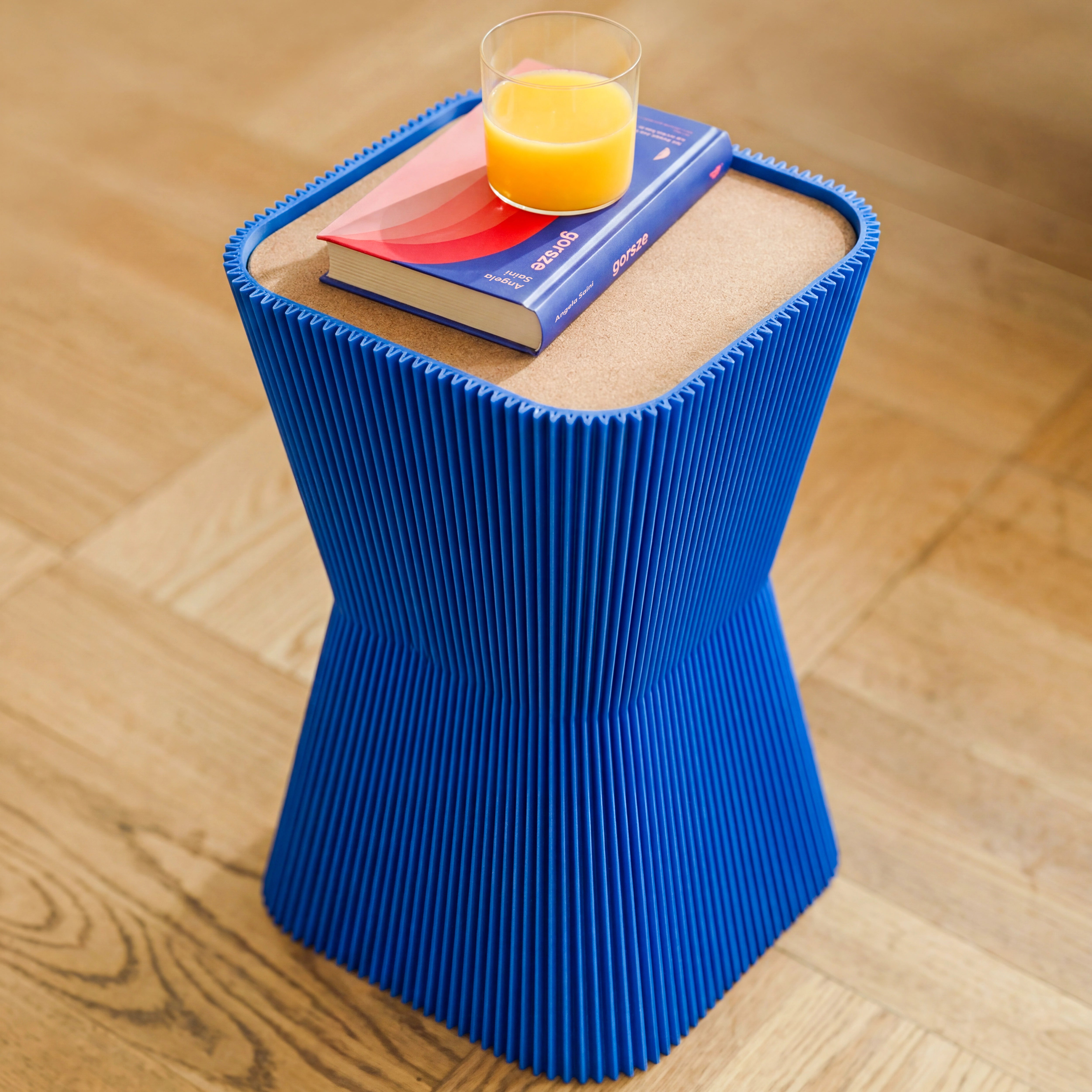 Detail des blauen Beistelltisches Pyramide mit Korkplatte, Buch und Glas Orangensaft auf Parkett