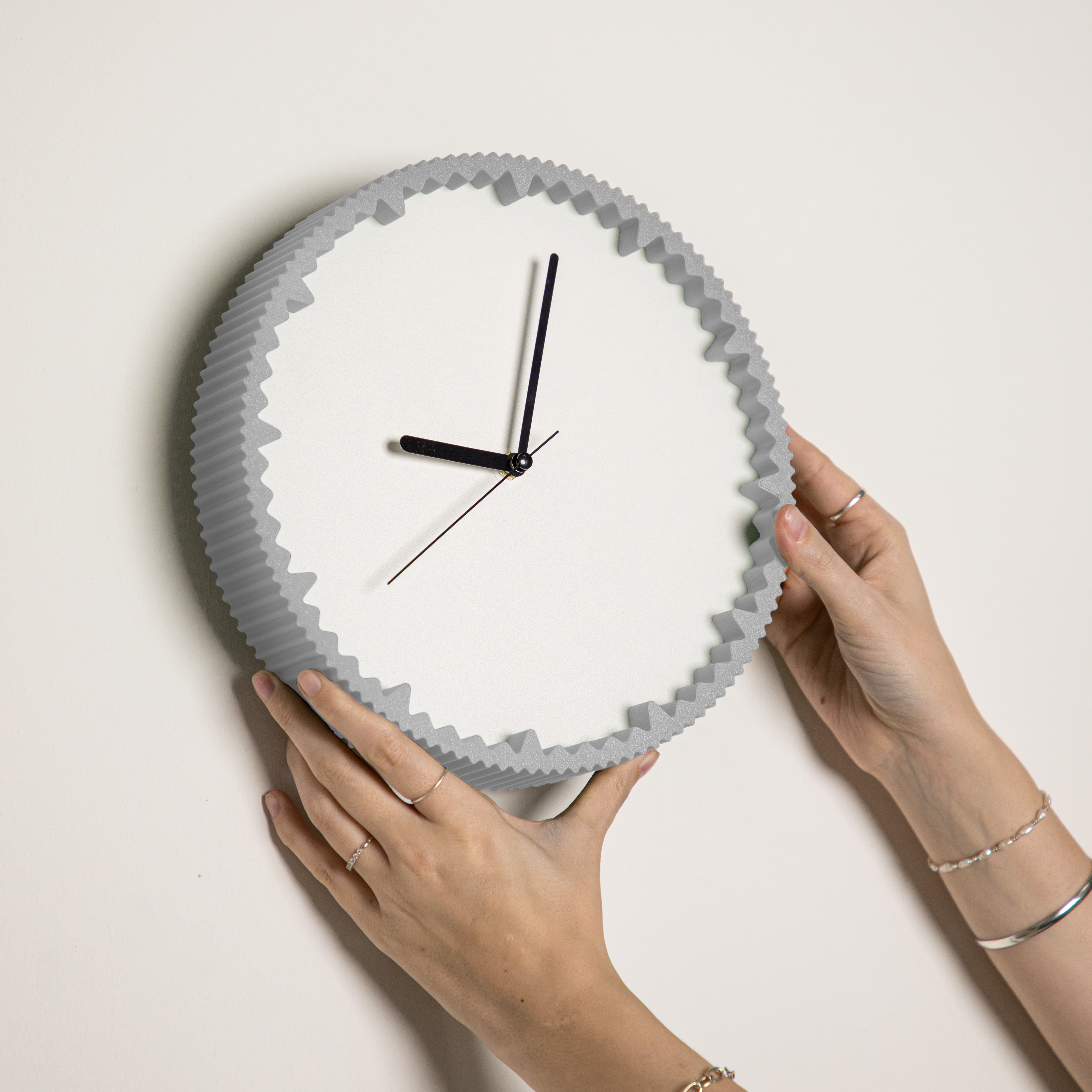 Hände hängen moderne Wanduhr grau mit gezacktem Rand aus dem 3D Druck an die Wand #farbe_hellgrau