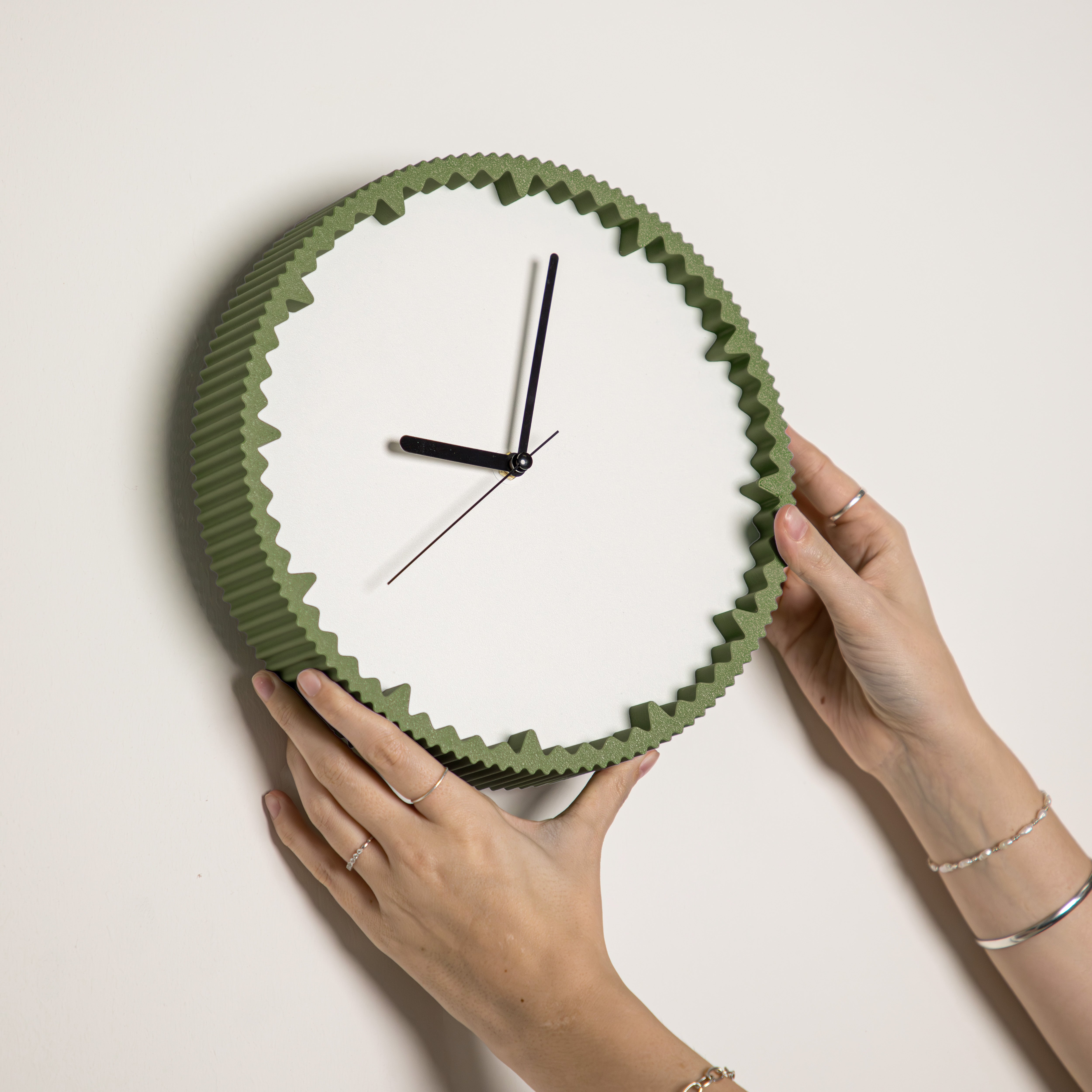Hände hängen moderne Wanduhr tannengrün mit gezacktem Rand aus dem 3D Druck an die Wand #farbe_olivgrün